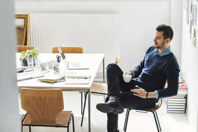 Mid adult businessman having coffee at desk in office