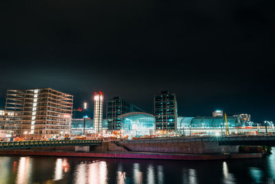 Illuminated buildings by river against sky at night