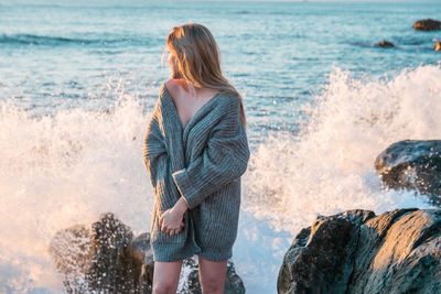 Rear view of woman standing on rock by sea