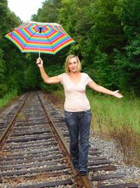 Full length portrait of woman with umbrella walking on railroad track