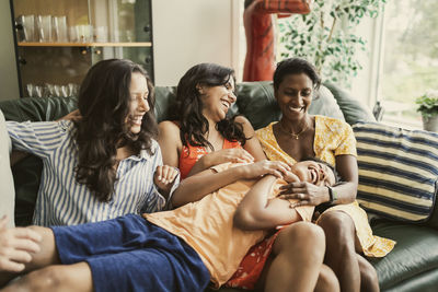 Happy mother and daughters playing with boy while sitting on sofa at home