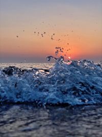 Water splashing on sea shore against sky during sunset