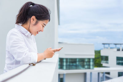 Side view of mid adult woman using smart phone while standing in balcony