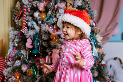 Funny child little girl in santa claus hat and pink dress laughs with happiness