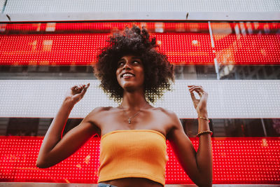 Low angle view of happy young woman standing against neon american flag in city