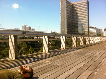 Man lying on footbridge against built structures