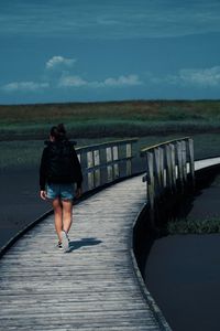 Rear view of woman standing on railing against sky