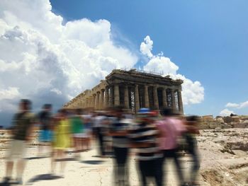 Blurred motion of people walking in city against cloudy sky