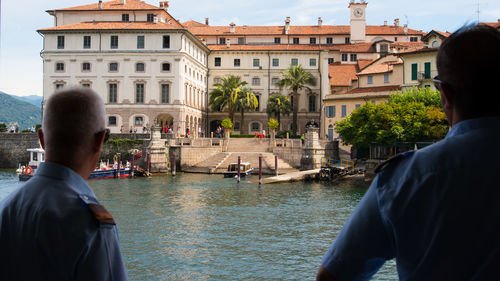 Rear view of man standing on river against buildings in city