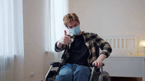 Portrait of man wearing mask gesturing while sitting on wheelchair