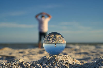 Close-up of crystal ball on rock at beach against sky