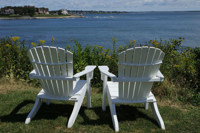 Empty chairs on field by sea