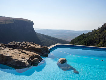 Scenic view of swimming pool at edge of mountain cliff against clear sky