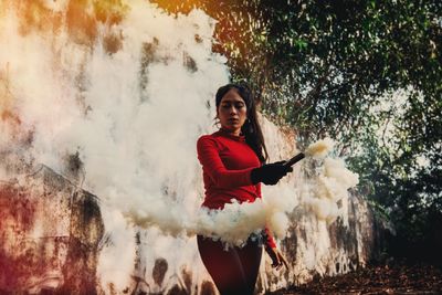 Young woman holding distress flare by wall