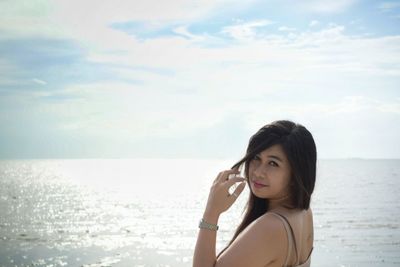 Portrait of young woman standing at beach against cloudy sky during sunny day