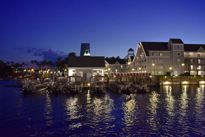 Illuminated buildings by river against sky at night