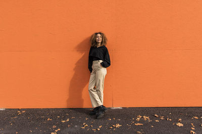 Woman with hand in pocket leaning on orange wall