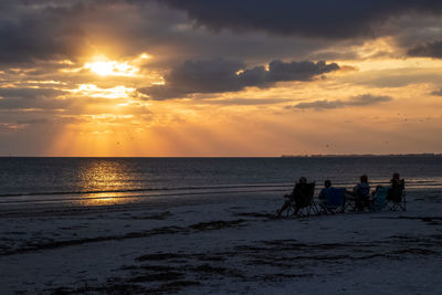 People sitting on sea against sky during sunset