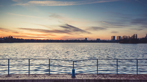 Scenic view of river by buildings against sky during sunset