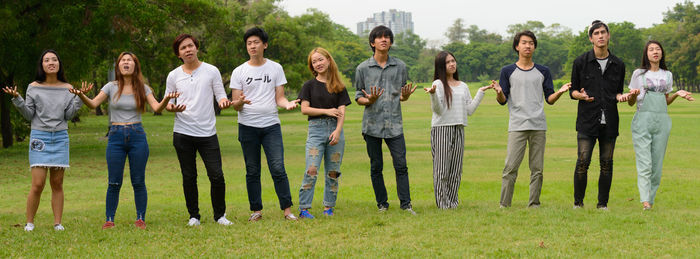 Group of people standing on grassland against trees