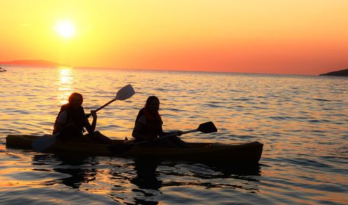 Silhouette people in boat on sea against sunset sky