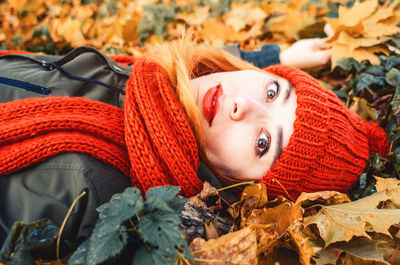 Autumn portrait of cute girl in orange warm knitted hat and orange scarf lying in fallen leaves 