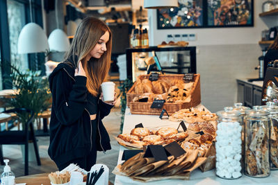 Woman holding cup with coffee looking at pastry, buns, cakes and cookies. girl buying a sweet food