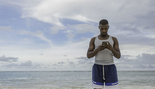 Portrait of young man standing at beach against sky