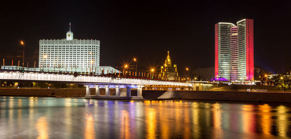 Illuminated bridge over river against buildings at night