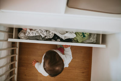 High angle view of baby girl standing by drawer at home