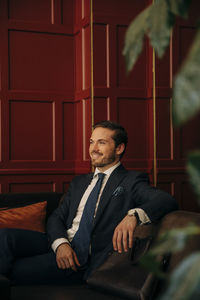 Smiling young businessman sitting on sofa in hotel lounge