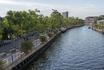 Bridge over river amidst trees and buildings in city against sky