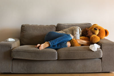 Full length of woman lying with teddy bear on sofa at home