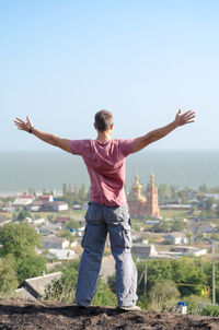 Rear view of man standing with arms outstretched against sky