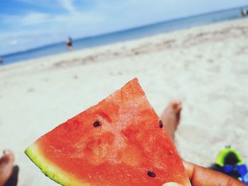 Close-up of hand holding fruit on beach against sky