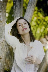 Portrait of young woman standing against tree trunk