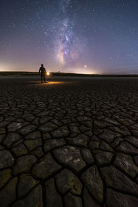 Back view of anonymous man standing on empty road with lantern on a colorful nigh sky with milky way on background