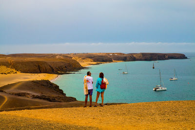 Rear view of people standing on shore against sky