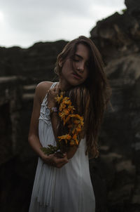 Young woman with flower standing against sky