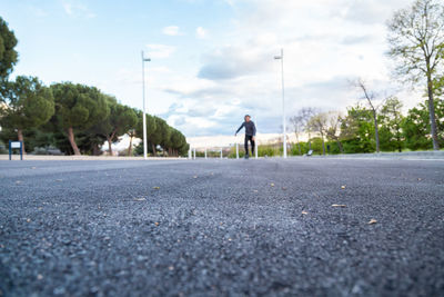 Surface level of young man skating on road against cloudy sky