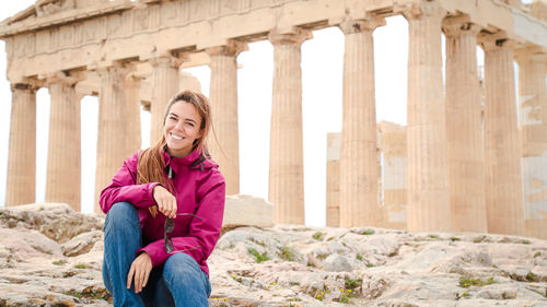 Portrait of smiling woman sitting against built structure