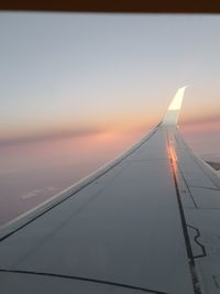 Airplane wing against sky during sunset