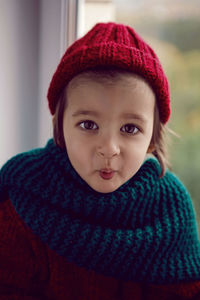 Boy child in red knitted sweater and hat sitting on the window in autumn