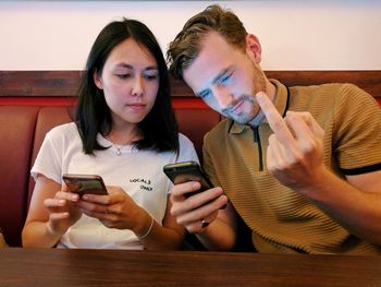 Man showing middle finger while sitting by female friend in restaurant