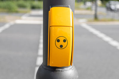 Close-up of yellow push button on pole by street