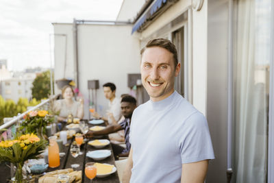 Portrait of smiling man with multiracial friends celebrating during dinner party in balcony