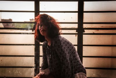 Young woman with tousled hair sitting against old window