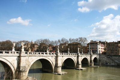 Arch bridge over river in city against sky