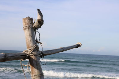 Bird perching on wooden post by sea against sky