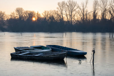 Boats in river against sky at sunset